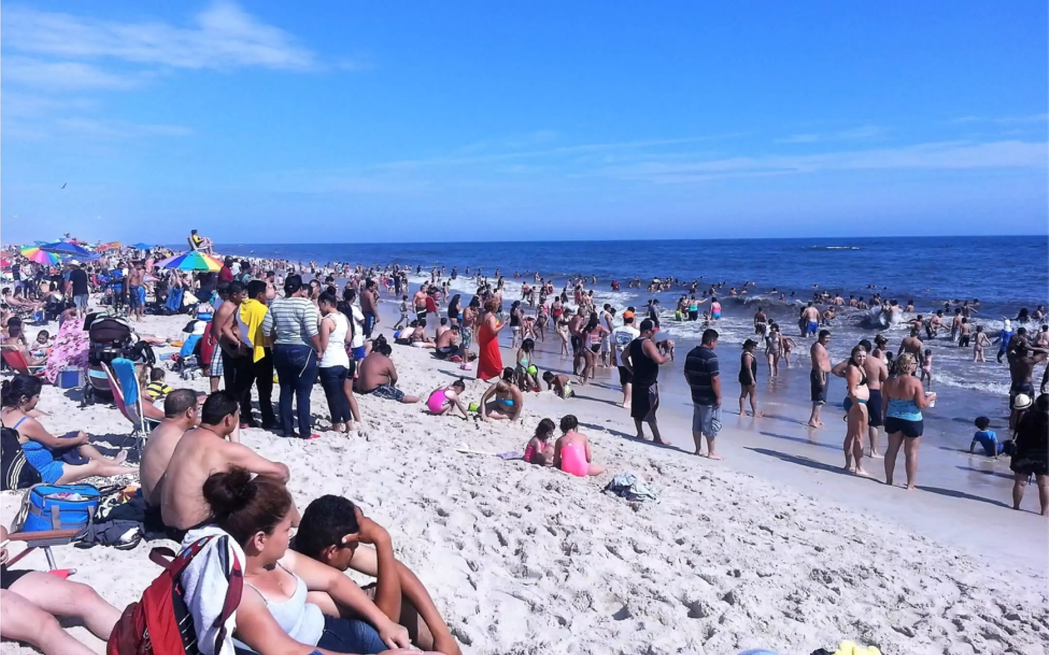 Crowded beach scene with people sunbathing and swimming